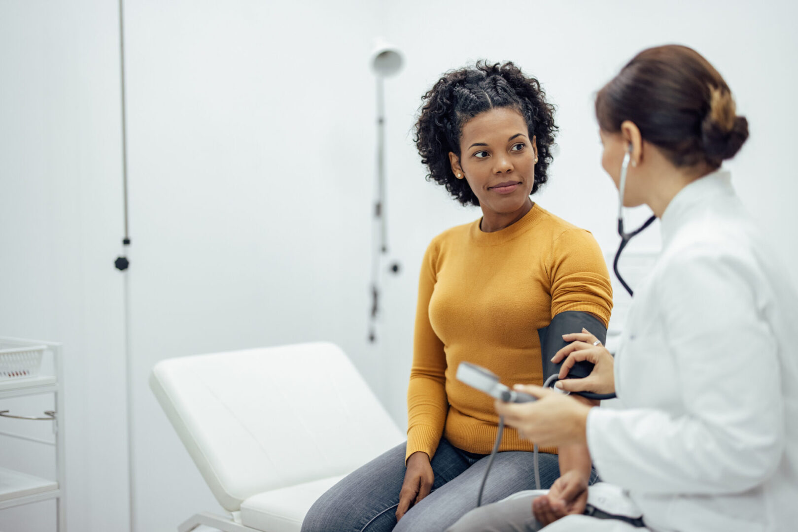 Woman sitting in a chair with a doctor standing beside her, holding a stethoscope and a device