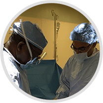 Two surgeons wearing masks, caps, and spectacles performing surgery in an operating room