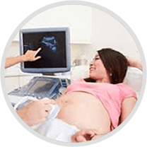 Pregnant woman lying on a bed, with a person's hand pointing to an ultrasound machine in the background